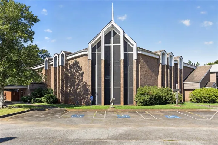 Brick exterior with a prominent steeple, large fenestration, multiple gabled rooflines, and an expansive paved parking area
