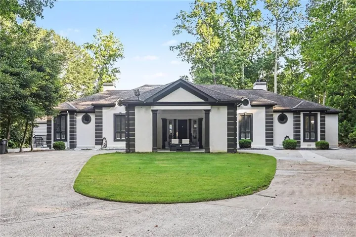 Contemporary ranch-style exterior with a covered entry, white stucco finish, dark trim accents, and a circular driveway