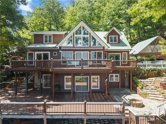 Multi-level deck with wood railing, large A-frame windows, covered boat dock, stone patio, and a stone fire pit