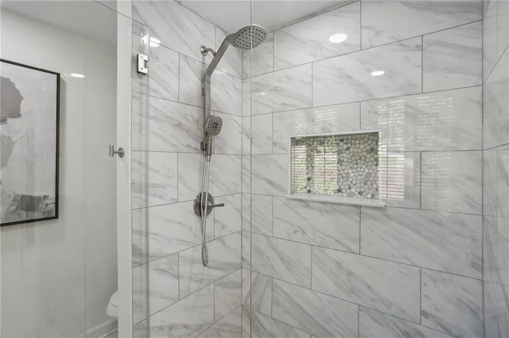 Primary bathroom with glass shower enclosure, brushed nickel fixture and tile finishes on both walls and floors.