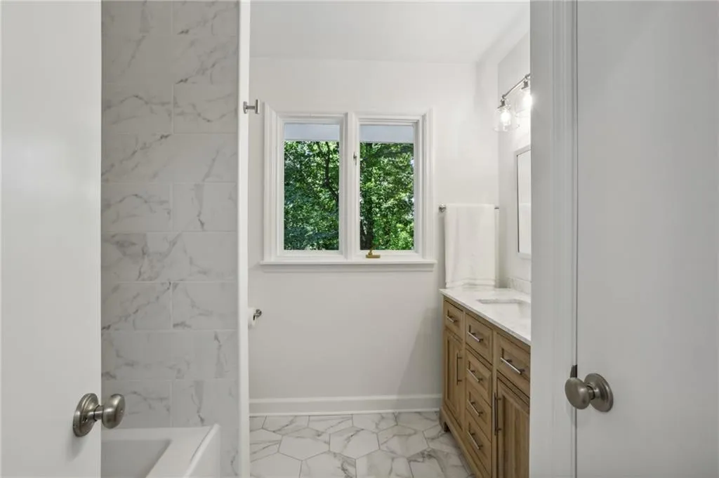 Fully renovated hall bath with wood vanity, tiled floor, tub and shower.