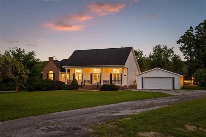 Traditional-style residence featuring a prominent front porch with columns, a dark shingled roof, and a red brick chimney