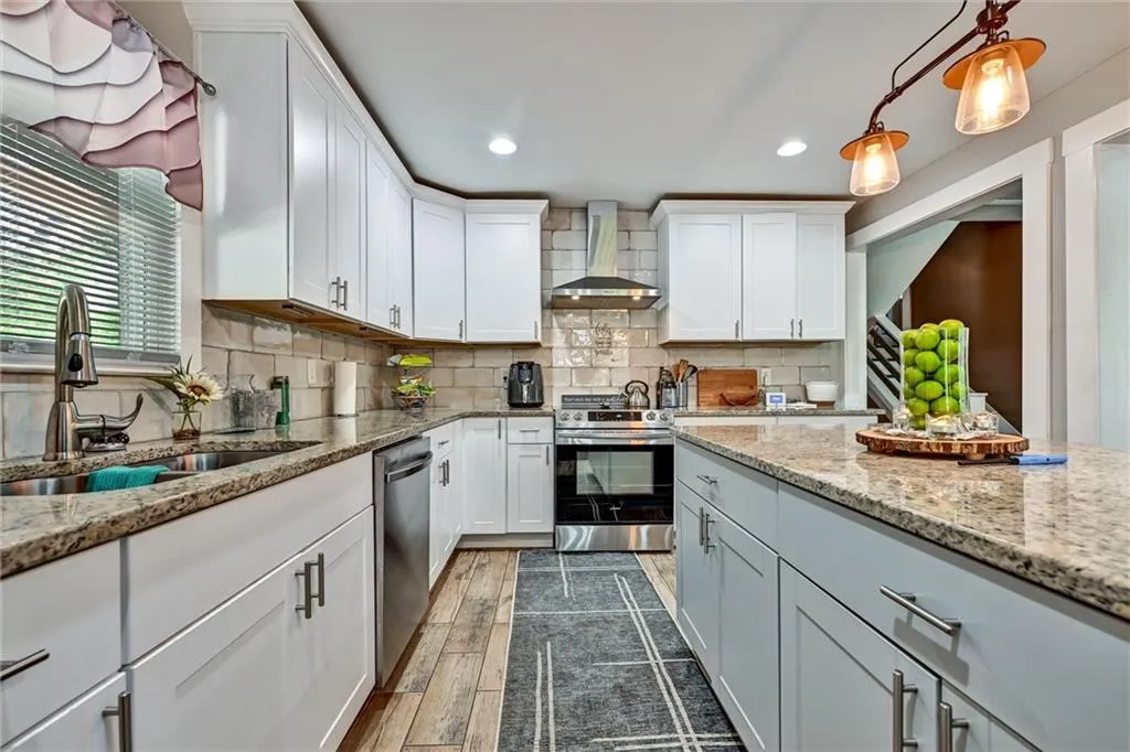 Kitchen featuring backsplash, appliances with stainless steel finishes, dark wood-type flooring, a sink, and wall chimney exhaust hood