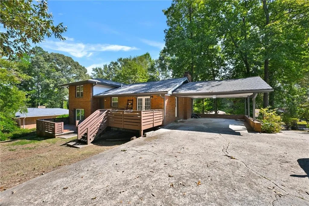 Split level home featuring a deck, aphalt driveway, an attached carport, brick siding, and a chimney
