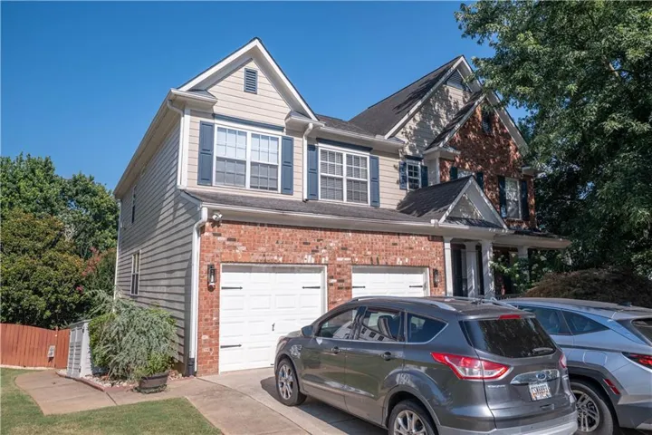 Two-story residential exterior featuring a brick and siding facade, a two-car garage with white doors, and a covered front entry with white columns