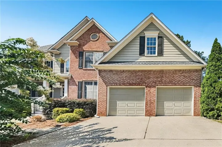 Brick and siding exterior with gabled roofs, two-car garage, mature landscaping, and an inviting front porch