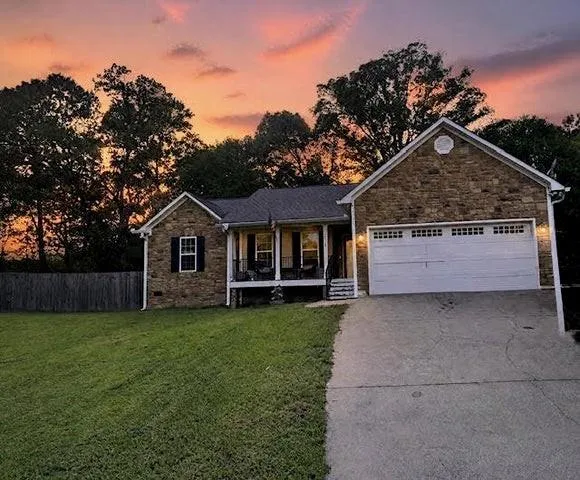Stone veneer exterior with a covered front porch, attached garage, and a concrete driveway