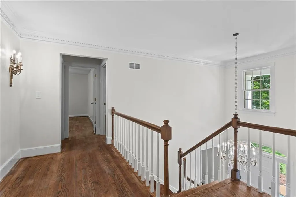 Upstairs landing with hardwood floors, detailed crown molding, and a view of the chandelier in the two-story foyer.