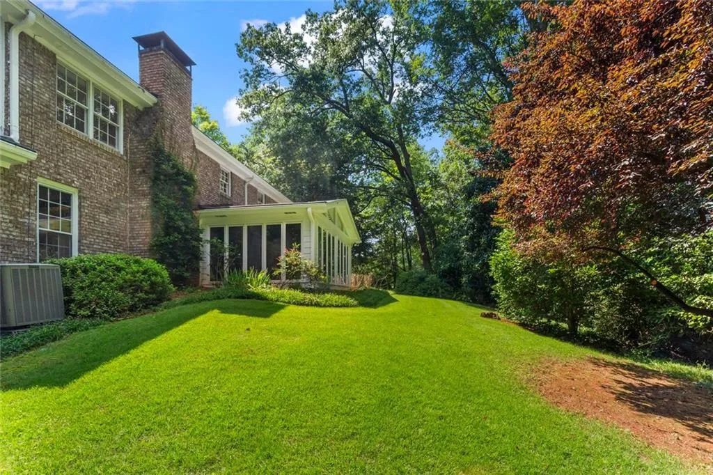 Back view of the home highlighting the spacious sunroom surrounded by a lush, private yard and mature trees.