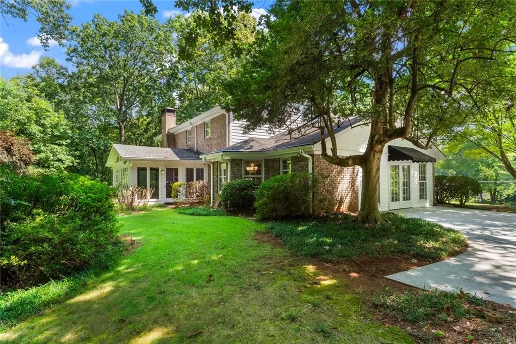 Side and back view of the home showcasing the bright sunroom surrounded by greenery and mature trees.