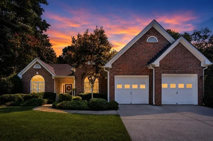 Brick exterior, arched windows, attached two-car garage, concrete driveway, and established landscaping