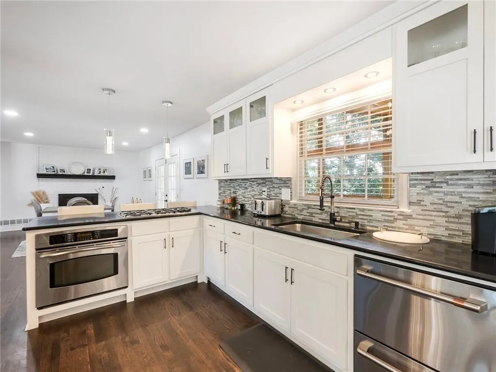 Kitchen featuring dark hardwood / wood-style flooring, appliances with stainless steel finishes, sink, decorative backsplash, and kitchen peninsula