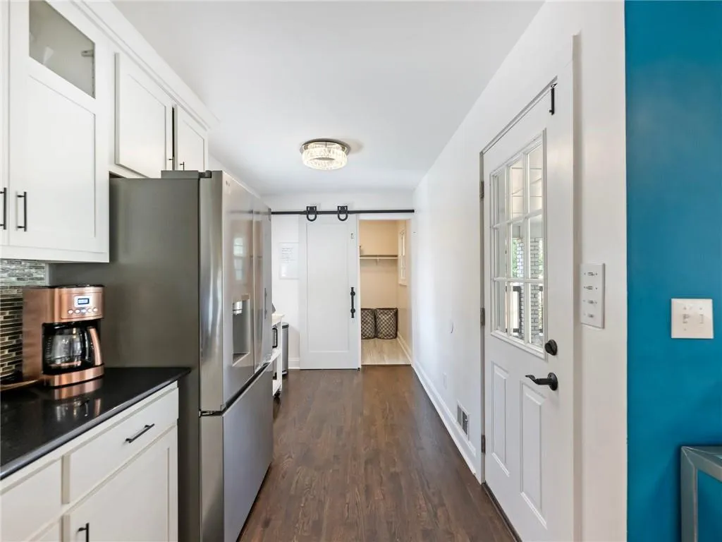Kitchen with a barn door, dark hardwood / wood-style flooring, white cabinetry, and decorative backsplash