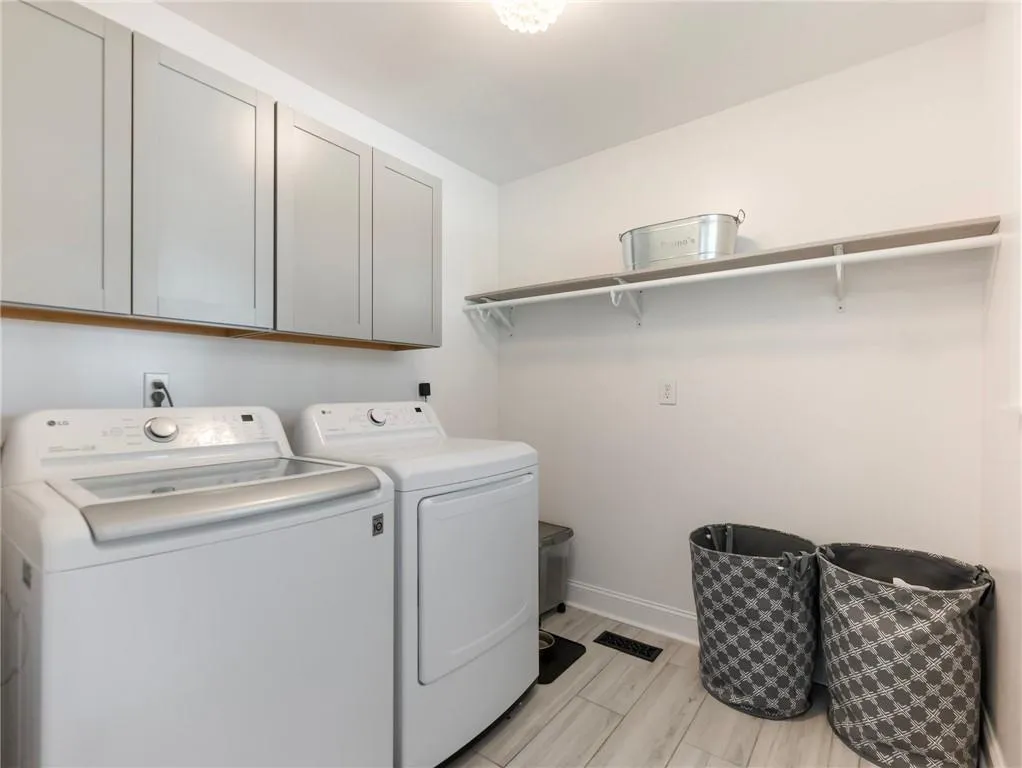 Clothes washing area featuring cabinets, washing machine and clothes dryer, and light wood-type flooring