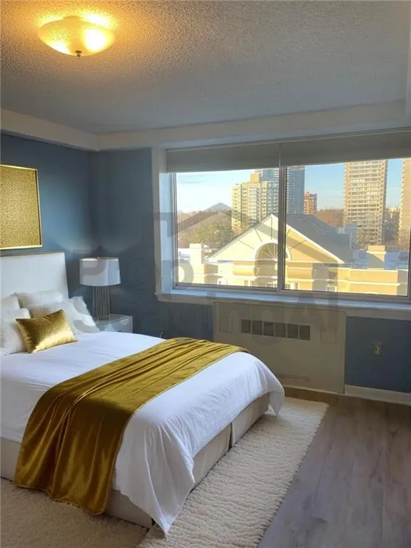 Bedroom featuring multiple windows, radiator heating unit, a textured ceiling, and wood finished floors.Look at AI Staging what thing could be like with a vision!