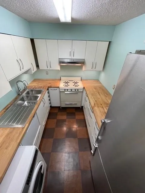 Kitchen with wooden counters, white stove, stainless steel refrigerator, white cabinetry, and a textured ceiling