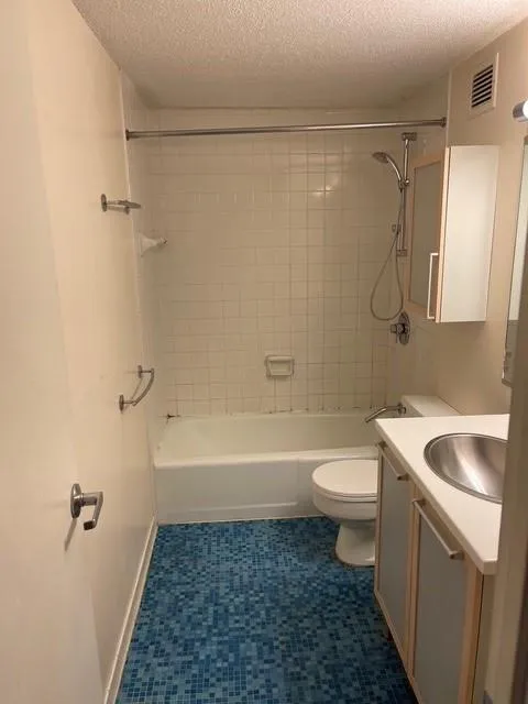 Full bathroom featuring a textured ceiling, toilet, vanity, and tiled shower / bath combo
