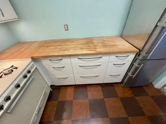 Kitchen with white range with gas cooktop, wood counters, white cabinetry, and stainless steel fridge