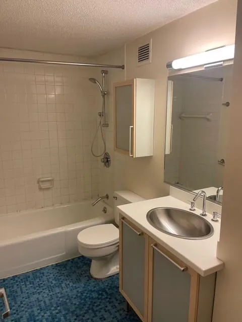 Full bathroom featuring a textured ceiling, tiled shower / bath combo, tile patterned floors, vanity, and toilet