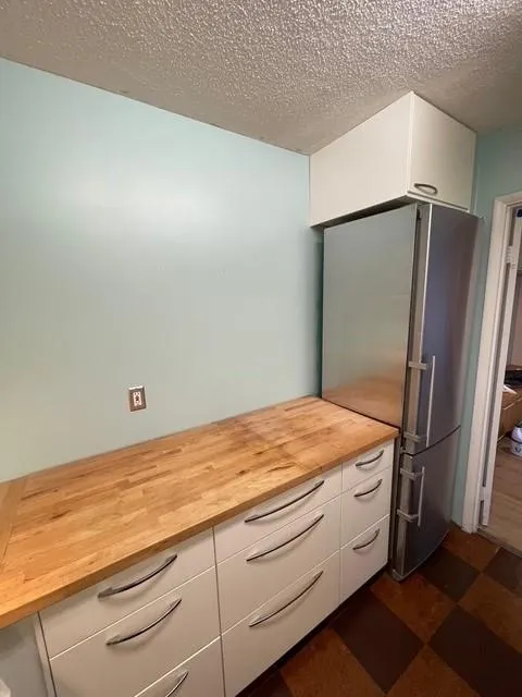 Kitchen with white cabinets, butcher block countertops, stainless steel fridge, and a textured ceiling