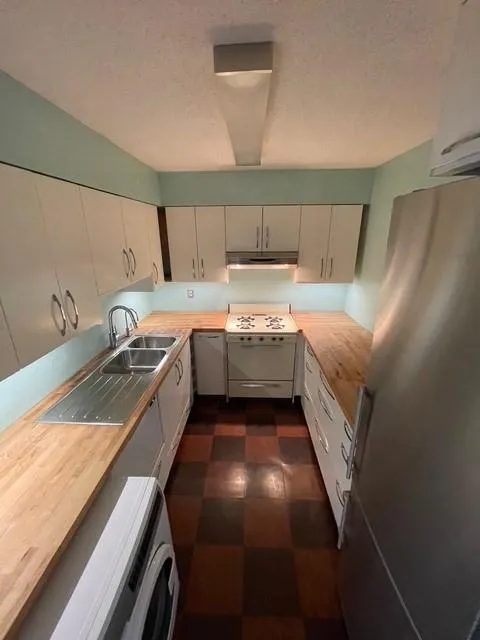 Kitchen with butcher block counters, stainless steel fridge, range, washer / clothes dryer, and sink