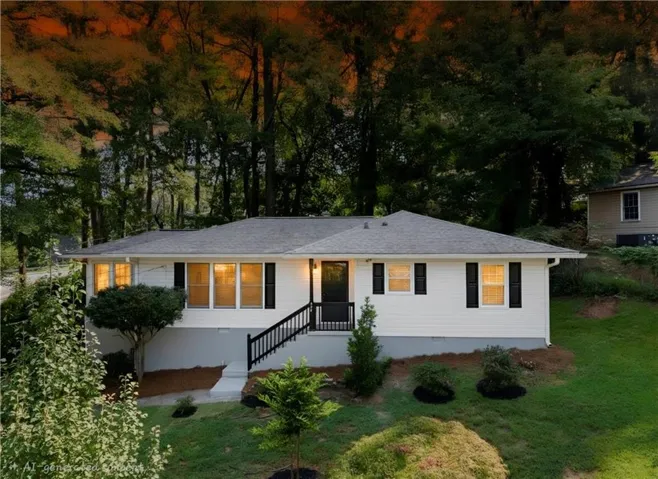 White exterior with dark shutters, front entry steps with dark railing, a gray shingle roof, and established landscaping