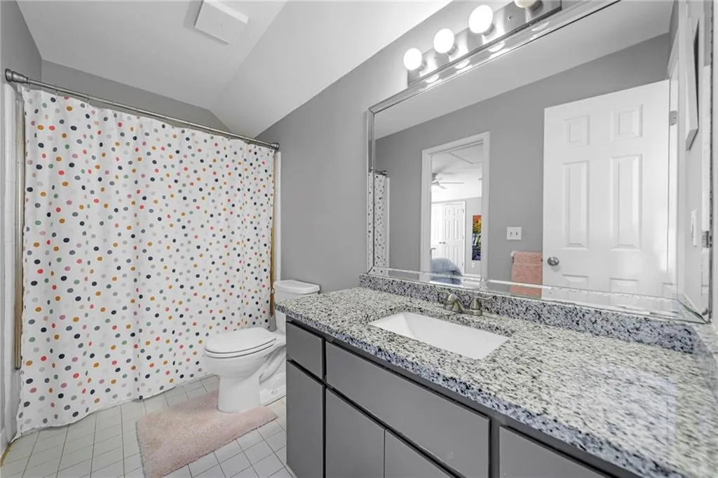 Bathroom with vanity with extensive cabinet space, lofted ceiling, ceiling fan, tile floors, and toilet