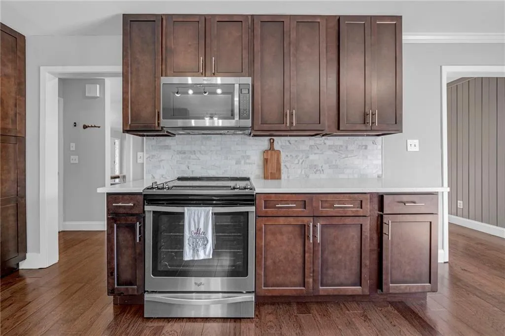 Kitchen with dark brown cabinets, crown molding, stainless steel appliances, dark hardwood / wood-style flooring, and tasteful backsplash