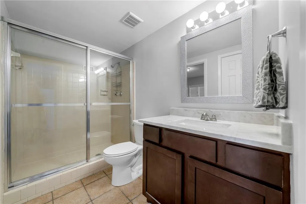 Bathroom featuring tile flooring, walk in shower, vanity, and toilet