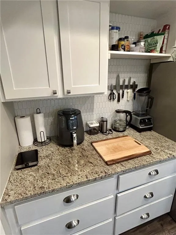 Kitchen featuring decorative backsplash, light stone counters, and white cabinetry