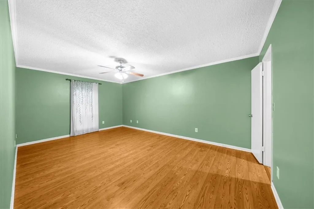 Empty room with crown molding, ceiling fan, light hardwood / wood-style floors, and a textured ceiling Empty room with crown molding, ceiling fan, light hardwood / wood-style floors, and a textured ceiling