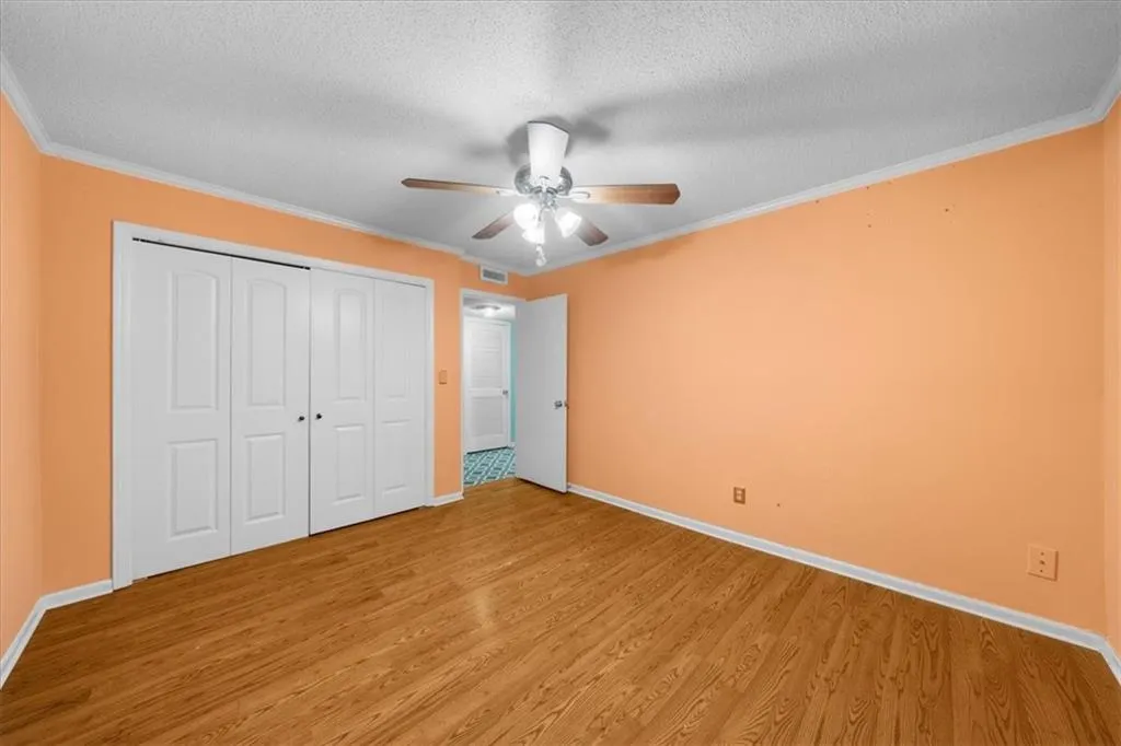 Unfurnished bedroom with hardwood / wood-style floors, ceiling fan, ornamental molding, and a textured ceiling Unfurnished bedroom with hardwood / wood-style floors, ceiling fan, ornamental molding, and a textured ceiling