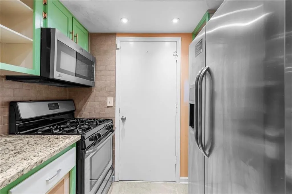 Kitchen with tasteful backsplash, stainless steel appliances, light stone counters, and green cabinetry Kitchen with tasteful backsplash, stainless steel appliances, light stone counters, and green cabinetry
