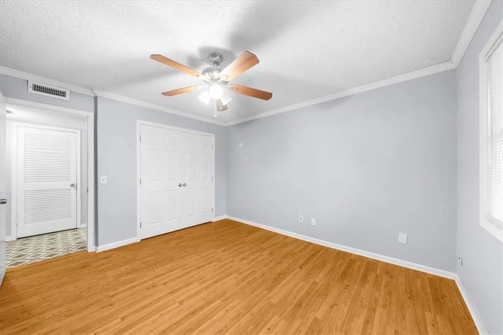 Unfurnished bedroom featuring ceiling fan, ornamental molding, a textured ceiling, wood-type flooring, and a closet Unfurnished bedroom featuring ceiling fan, ornamental molding, a textured ceiling, wood-type flooring, and a closet