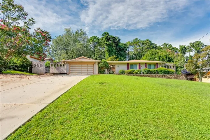 Expansive front lawn, two-car garage, mature trees, concrete driveway, and a stone-faced retaining wall