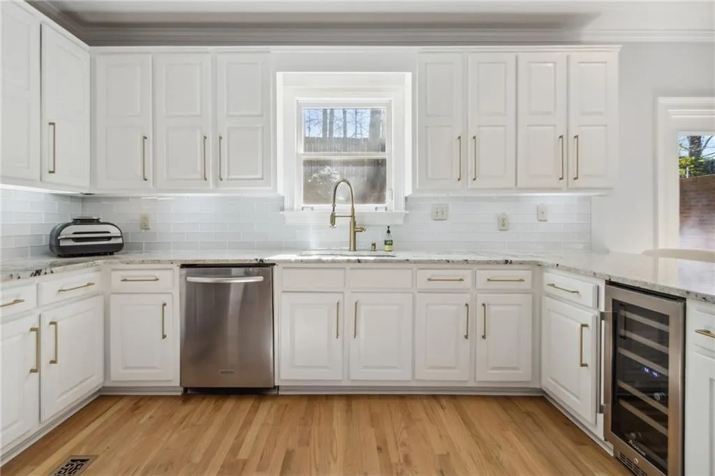 Kitchen featuring light wood-type flooring, sink, stainless steel dishwasher, and white cabinetry