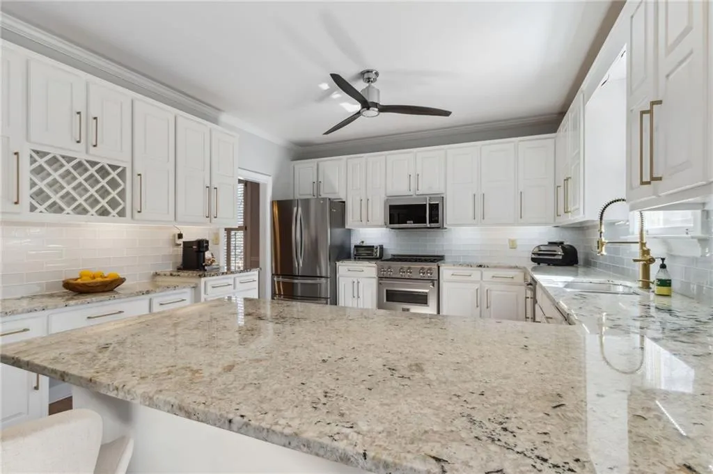 Kitchen with ceiling fan, crown molding, white cabinets, stainless steel appliances, and backsplash