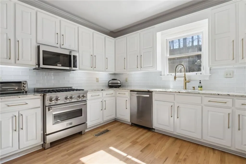 Kitchen featuring light hardwood / wood-style floors, backsplash, appliances with stainless steel finishes, light stone countertops, and white cabinetry