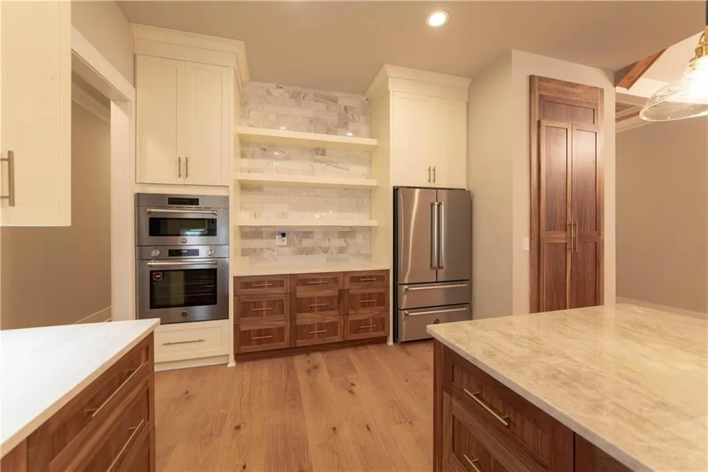Kitchen with light wood-type flooring, tasteful backsplash, light stone counters, white cabinetry, and stainless steel appliances