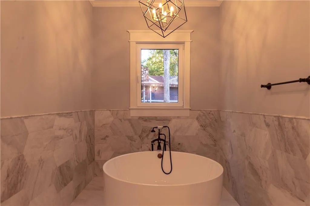 Bathroom with a washtub, ornamental molding, tile walls, and an inviting chandelier