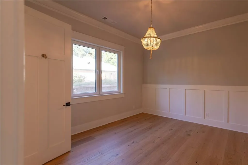 Empty room with light hardwood / wood-style floors, an inviting chandelier, and ornamental molding