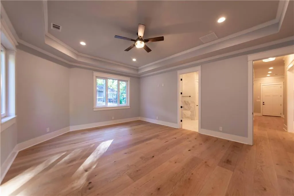 Empty room with ceiling fan, a raised ceiling, ornamental molding, and light hardwood / wood-style flooring