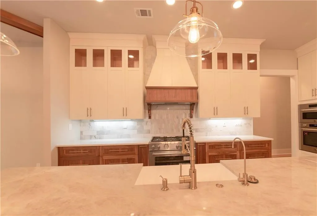 Kitchen with hanging light fixtures, stainless steel appliances, premium range hood, decorative backsplash, and white cabinets