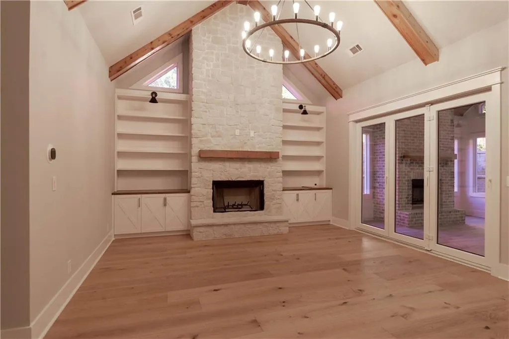 Unfurnished living room with a fireplace, wood-type flooring, a chandelier, and beamed ceiling