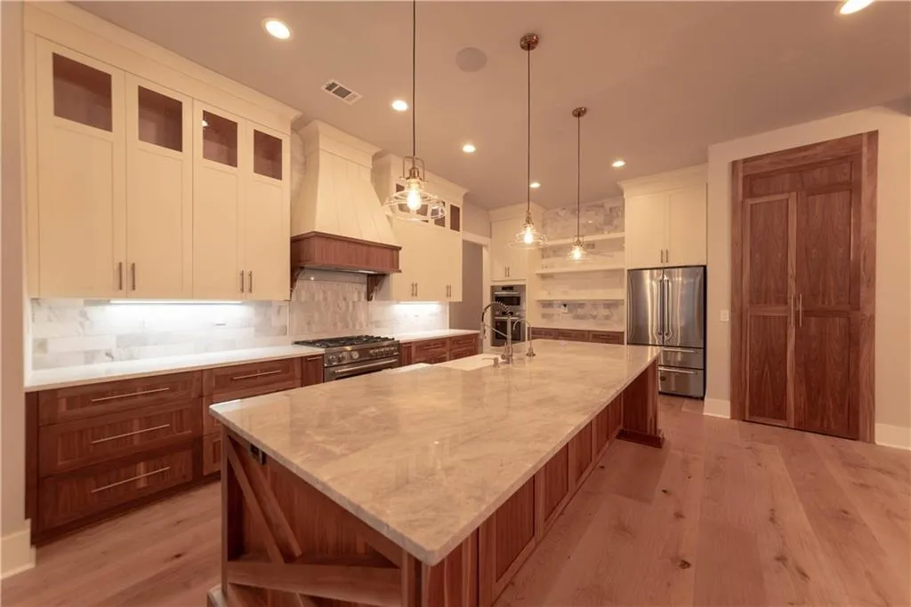 Kitchen featuring premium range hood, a spacious island, appliances with stainless steel finishes, decorative light fixtures, and white cabinetry