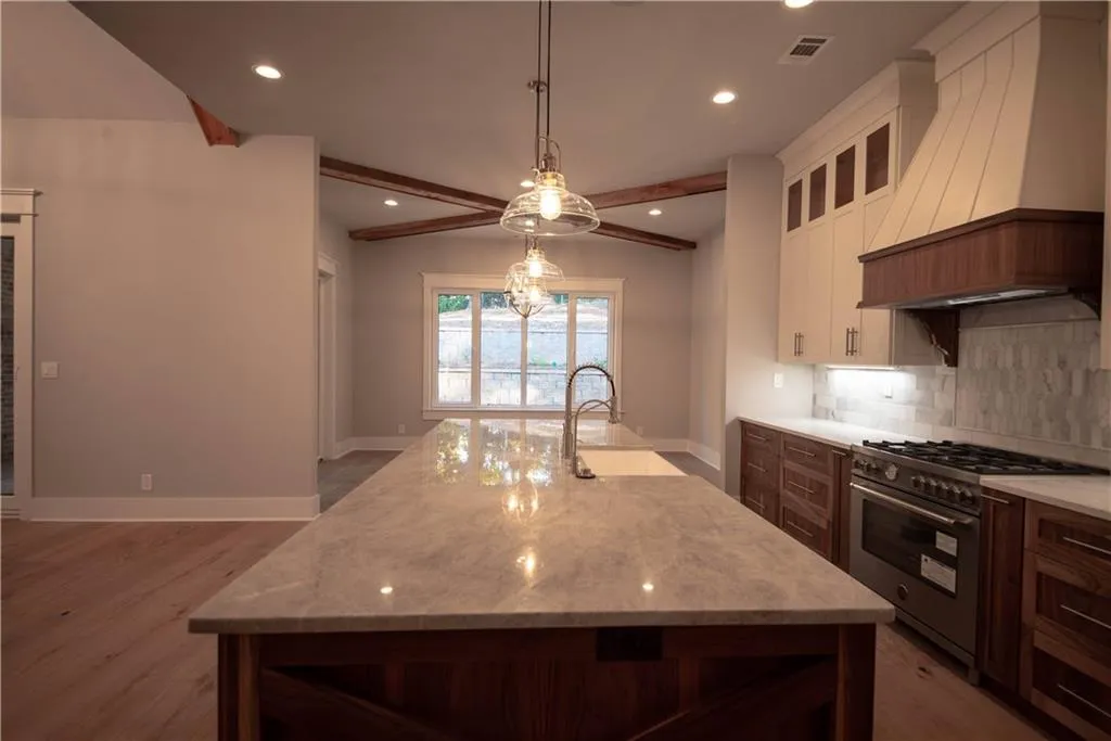 Kitchen featuring premium range hood, white cabinets, a center island with sink, high end stainless steel range, and beam ceiling