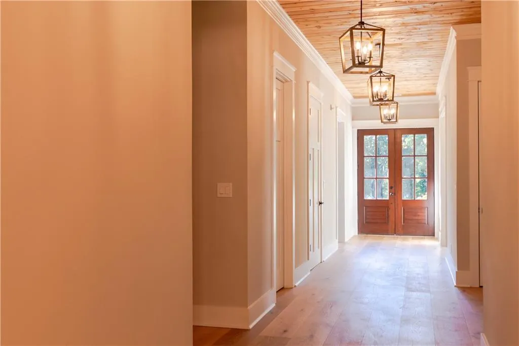 Hallway with french doors, wood ceiling, crown molding, a notable chandelier, and light hardwood / wood-style floors
