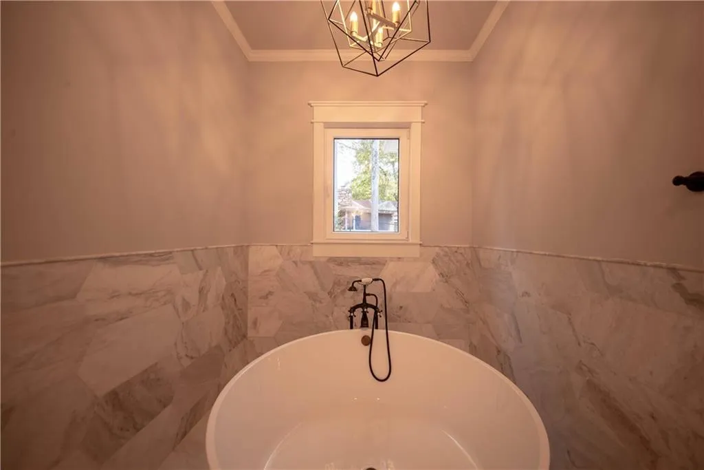 Bathroom with a bathtub, ornamental molding, tile walls, and an inviting chandelier