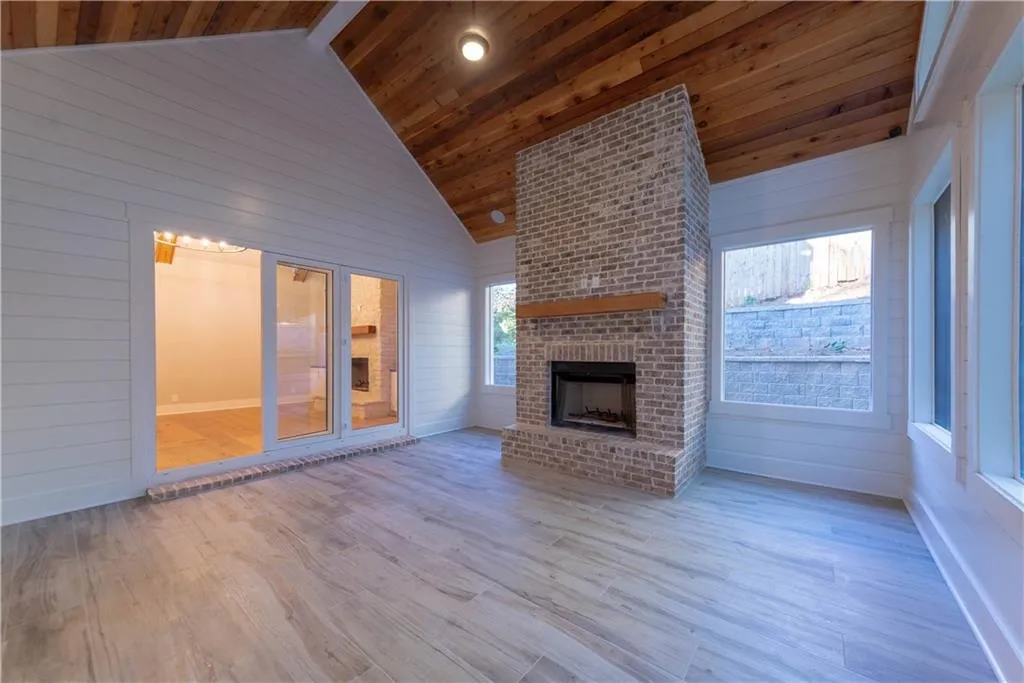 Unfurnished living room with an outdoor brick fireplace, light hardwood / wood-style floors, wood ceiling, and wooden walls