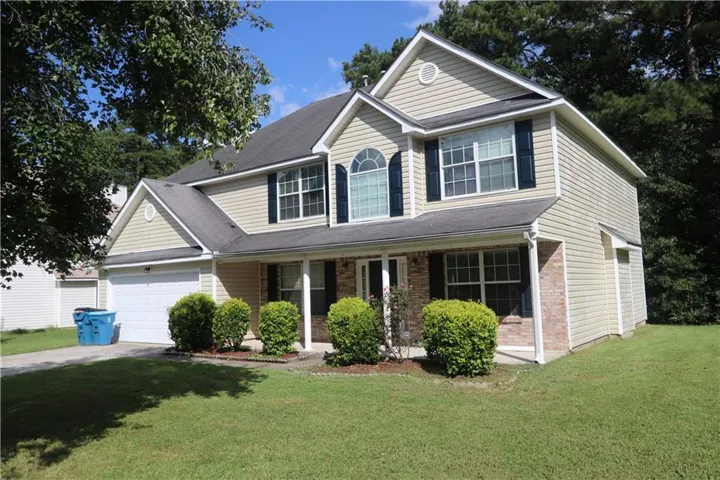 Two-story residence featuring light-colored siding, dark shutters, an arched window, and a covered front porch, complemented by a garage and a verdant lawn
